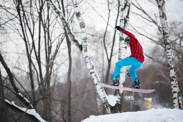 Image d'un sportif portant un casque chevauchant du snowboard sur une pente enneigée — Photo