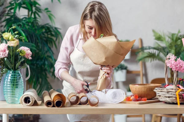 Foto de florista mujer en delantal con ramo de papel kraft a la mesa con papel con mermelada — Foto de Stock