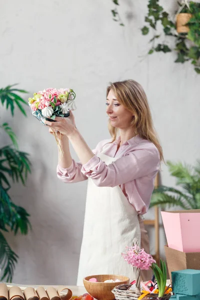 Фото флориста, держащего букет в руках за столом с мармеладом, зефиром, коробками, бумагой — стоковое фото