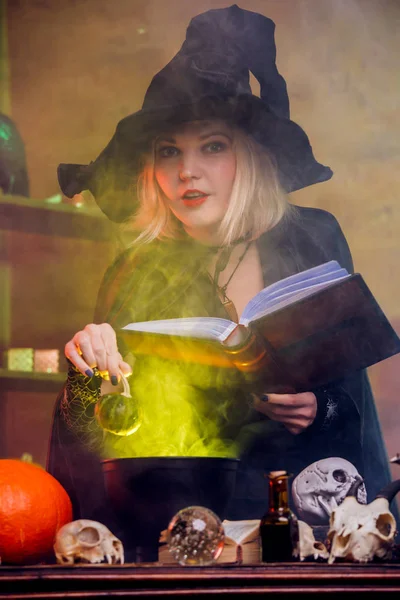 Photo de jeune sorcière en chapeau noir avec potion de brassage de livres en pot — Photo