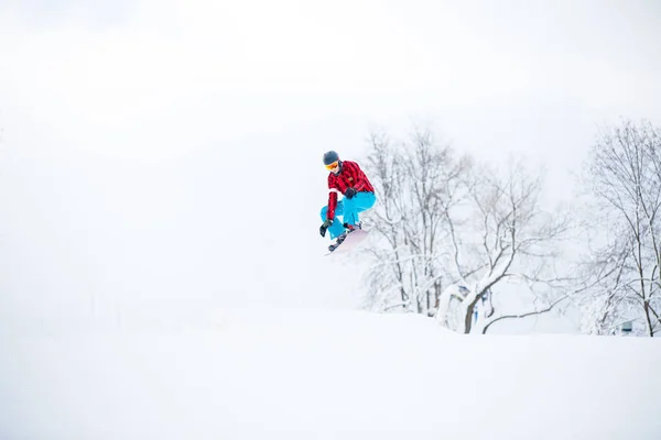 Snowboardista muž skákání na zasněžené kopce — Stock fotografie