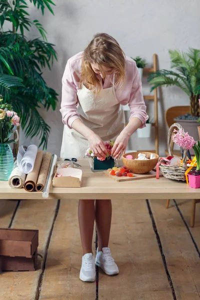 Фото флористки в фартуке с зефиром, мармеладом за столом — стоковое фото