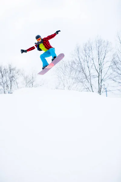 Photo de sportif en casque avec saut en snowboard en station enneigée — Photo