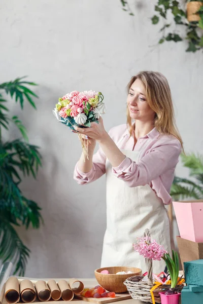 Foto van bloemist bedrijf boeket in handen aan tafel met marmelade, marshmallow, dozen, papier — Stockfoto