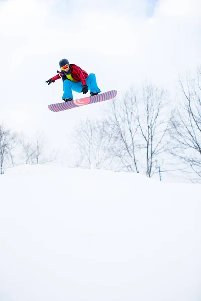 Imagen de hombre deportivo en casco con snowboard saltando en resort nevado —  Fotos de Stock