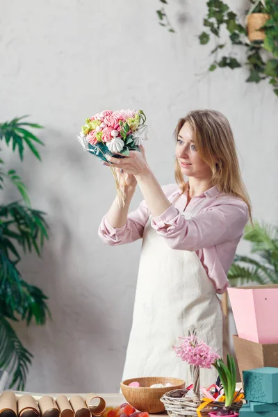 Portrait of florist holding bouquet in hands at table with marmalade, marshmallow, boxes, paper — Stock Photo, Image