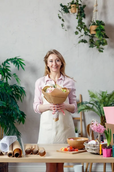 Foto de florista sonriente en delantal con ramo de flores con papel kraft — Foto de Stock