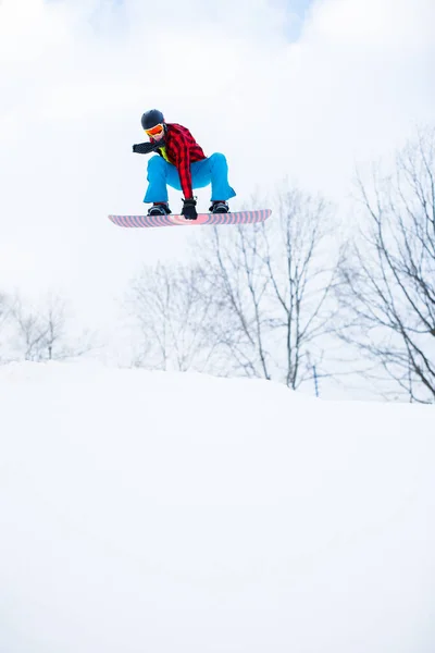 Imagem do atleta usando capacete com snowboard pulando em resort nevado — Fotografia de Stock