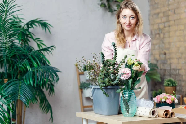 Foto van bloemist vrouw in schort met emmer met bloemen op tafel — Stockfoto