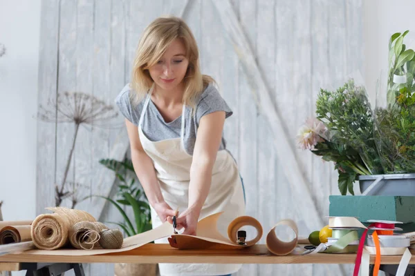 Blonde bloemist snijdt inpakpapier — Stockfoto