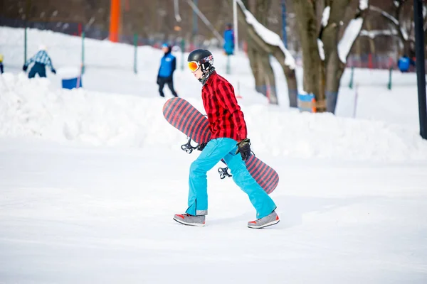 Foto de un hombre deportivo con snowboard caminando en un resort nevado — Foto de Stock