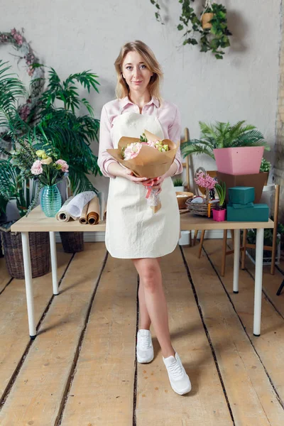 Foto de jovem florista em avental com buquê em mãos — Fotografia de Stock
