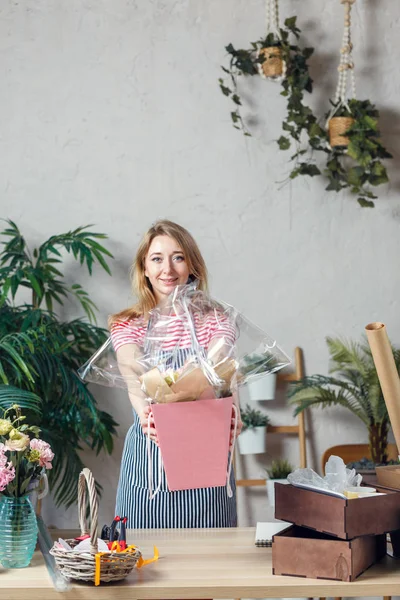 Foto de florista mujer con ramo en caja sobre fondo de plantas de interior — Foto de Stock