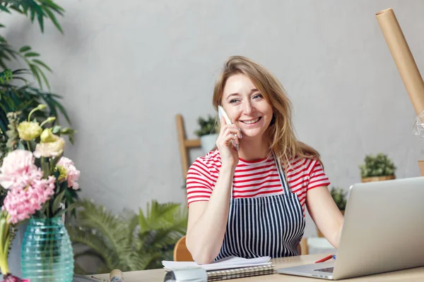 Porträtt av blond florist prata telefon sitter vid bord med dator — Stockfoto