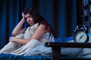 Yatakta çalar saat yanında oturan uykusuzluk ile mutsuz kadın fotoğrafı