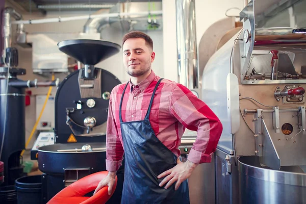 Foto de homem feliz no avental no fundo do moedor de café industrial — Fotografia de Stock