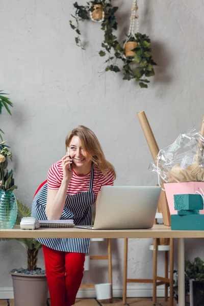 Foto van blonde bloemist praten over telefoon aan tafel met laptop — Stockfoto