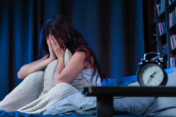 Álmatlanság ült az ágy mellett ébresztőórát a boldogtalan nő képe — Stock Fotó