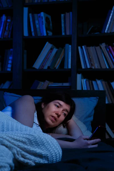 Portrait of woman with phone lying in bed at night — Stok Foto