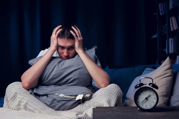Image of man with insomnia with pillow sitting next to alarm