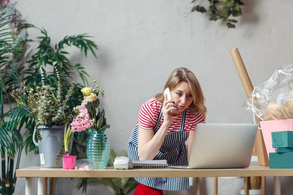 Picture of florist girl talking on phone while sitting at table with computer — Stock Photo, Image