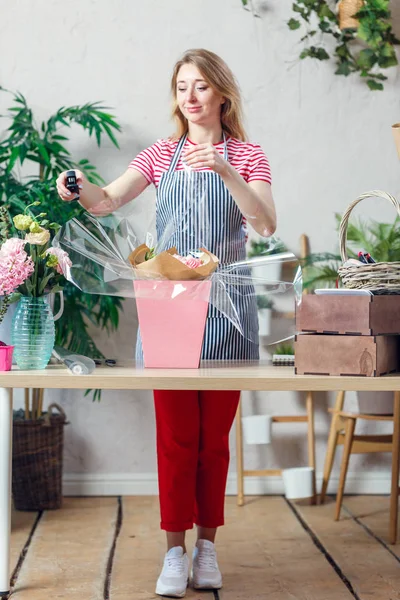 Photo of florist woman with stapler decorating flower arrangement at table with flowers, boxes — Stock Photo, Image