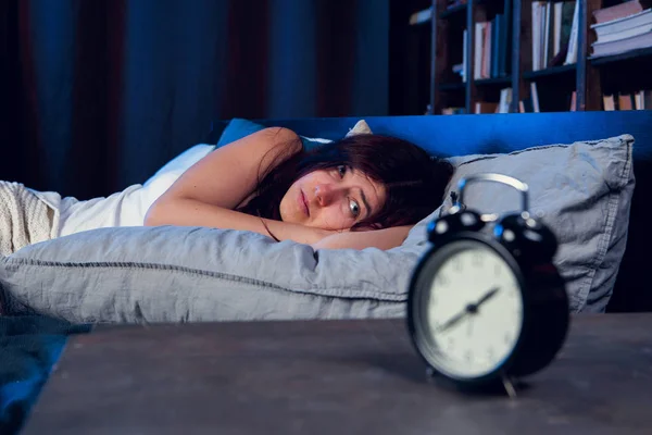 Portrait of dissatisfied woman with insomnia lying on bed next to alarm clock at night — Stock Photo, Image