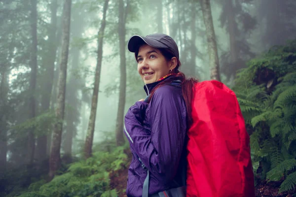 Foto de menina sorridente com mochila na floresta nebulosa — Fotografia de Stock