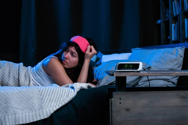 Immagine di giovane bruna con insonnia con benda rosa sull'occhio sdraiata sul letto accanto all'orologio — Foto Stock