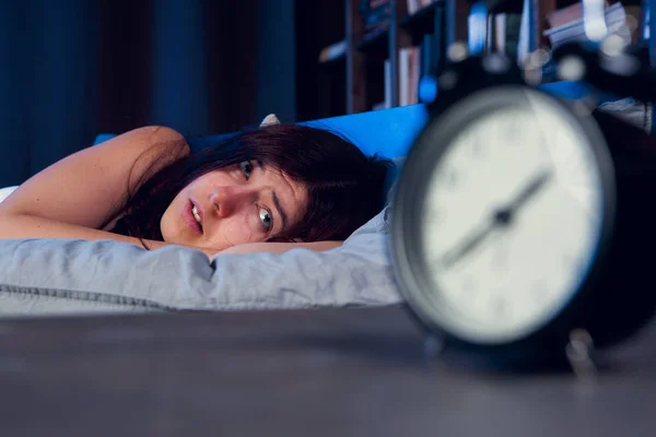 Obraz kobieta niezadowolony z bezsennością, leżąc na łóżku obok budzik nocą — Zdjęcie stockowe