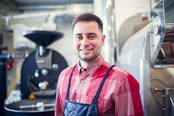 Portrait of young man in apron on background of industrial coffee grinder — Stock Photo, Image