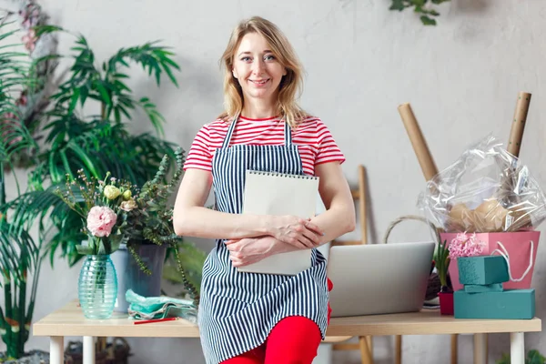 Foto de mujer sonriente sosteniendo floristería floral con cuaderno en blanco — Foto de Stock