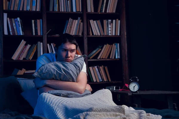 Фото людини з безсонням, що сидить у ліжку поруч з будильником — стокове фото