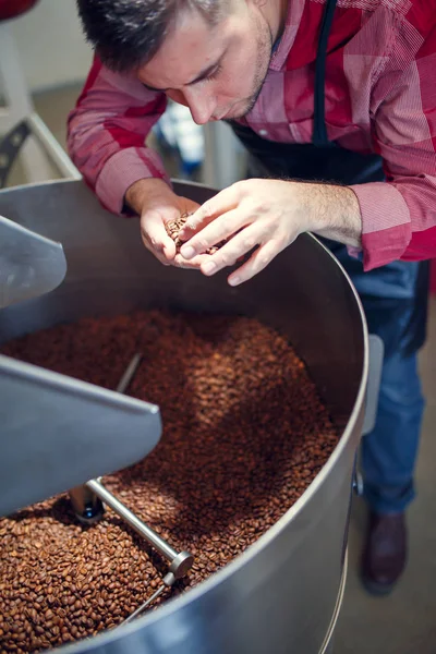 Imagem de jovem empresário com grãos de café na mão ao lado de torrador — Fotografia de Stock