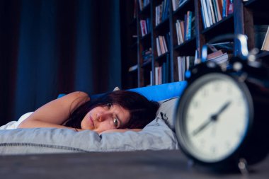 Geceleri yatağının çalar saat yanında yatan uykusuzluk ile esmer fotoğraf