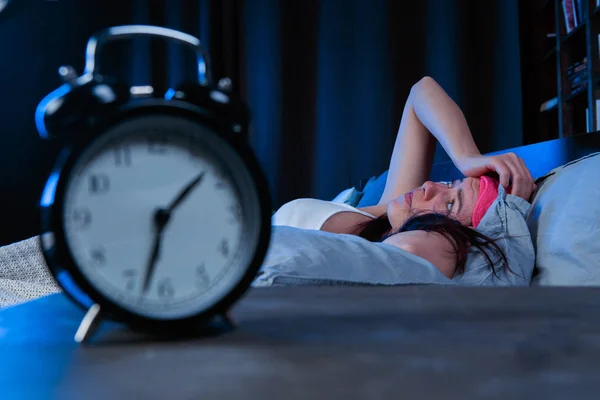 Gambar wanita dengan insomnia dengan perban mata merah muda tergeletak di tempat tidur di samping jam alarm — Stok Foto