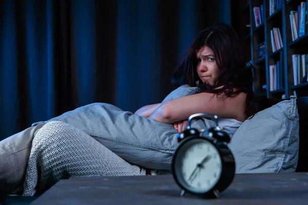 Retrato de chica insatisfecha con insomnio sentado en la cama al lado del despertador por la noche —  Fotos de Stock
