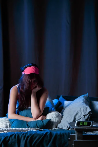 Image of young brunette with insomnia with pink bandage for eyes sitting on bed next to clock — Stock Photo, Image