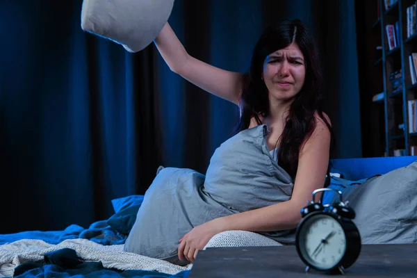 Elégedetlen nő álmatlanság fénykép dob párna ül az ágy mellett ébresztőórát — Stock Fotó