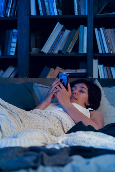 Изображение женщины с бессонницей с телефоном в руках, лежащей на кровати в спальне — стоковое фото