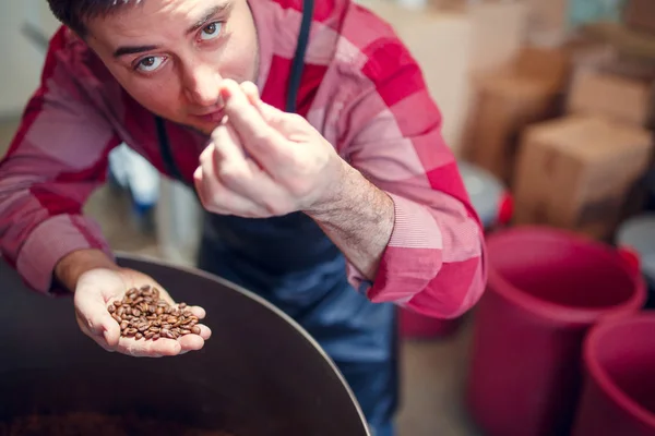 咖啡豆的年轻人的图片在手旁边烘烤机 — 图库照片