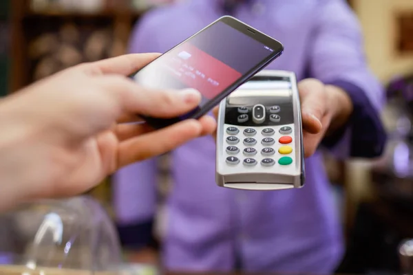 Fotografia cumpărătorului plătește cu smartphone-ul lângă vânzător cu terminal — Fotografie, imagine de stoc