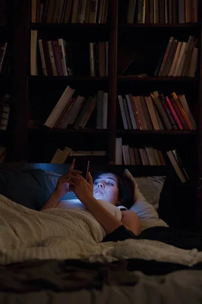 Imagen de mujer con teléfono acostada en la cama por la noche —  Fotos de Stock