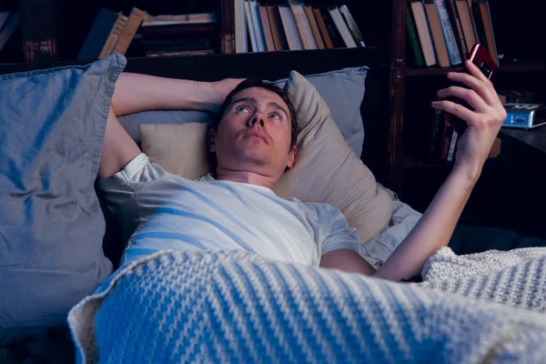 Obraz człowieka z bezsenność z telefonem w ręce, leżąc w łóżku — Zdjęcie stockowe