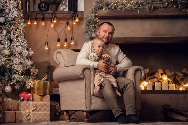 Foto di padre con suo figlio seduto in poltrona da albero di Capodanno e camino  . — Foto Stock