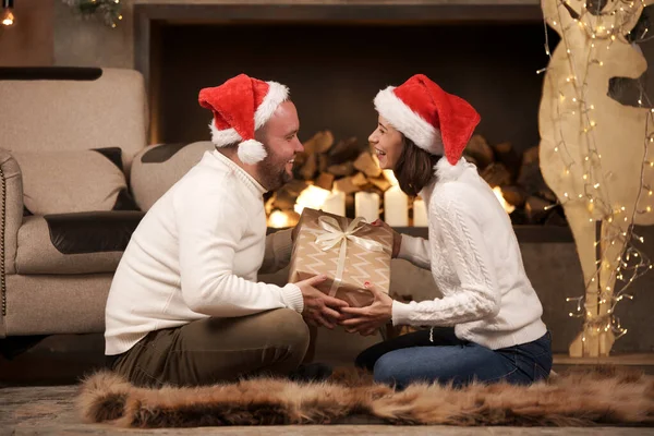 Φωτογραφία από την πλευρά του άνδρα και της γυναίκας στο Santas καλύμματα κάθεται στο πάτωμα στο δωμάτιο — Φωτογραφία Αρχείου