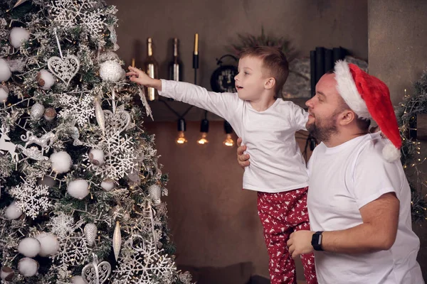 Foto de padre en gorra de Santas con su hijo cerca del abeto de Navidad . —  Fotos de Stock