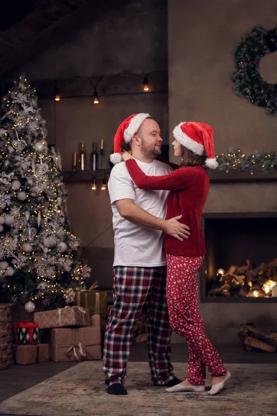 Retrato lateral de hombres y mujeres abrazados en gorra y pijama de Santas en la habitación — Foto de Stock