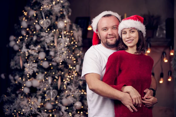 Photo of embracing men and women in Santas cap on background of Christmas tree — Stock Photo, Image