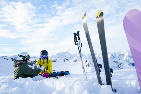 Image of skis, ski poles, snowboard against background of two sports women with thermos sitting in ski resort in winter — Stock Photo, Image
